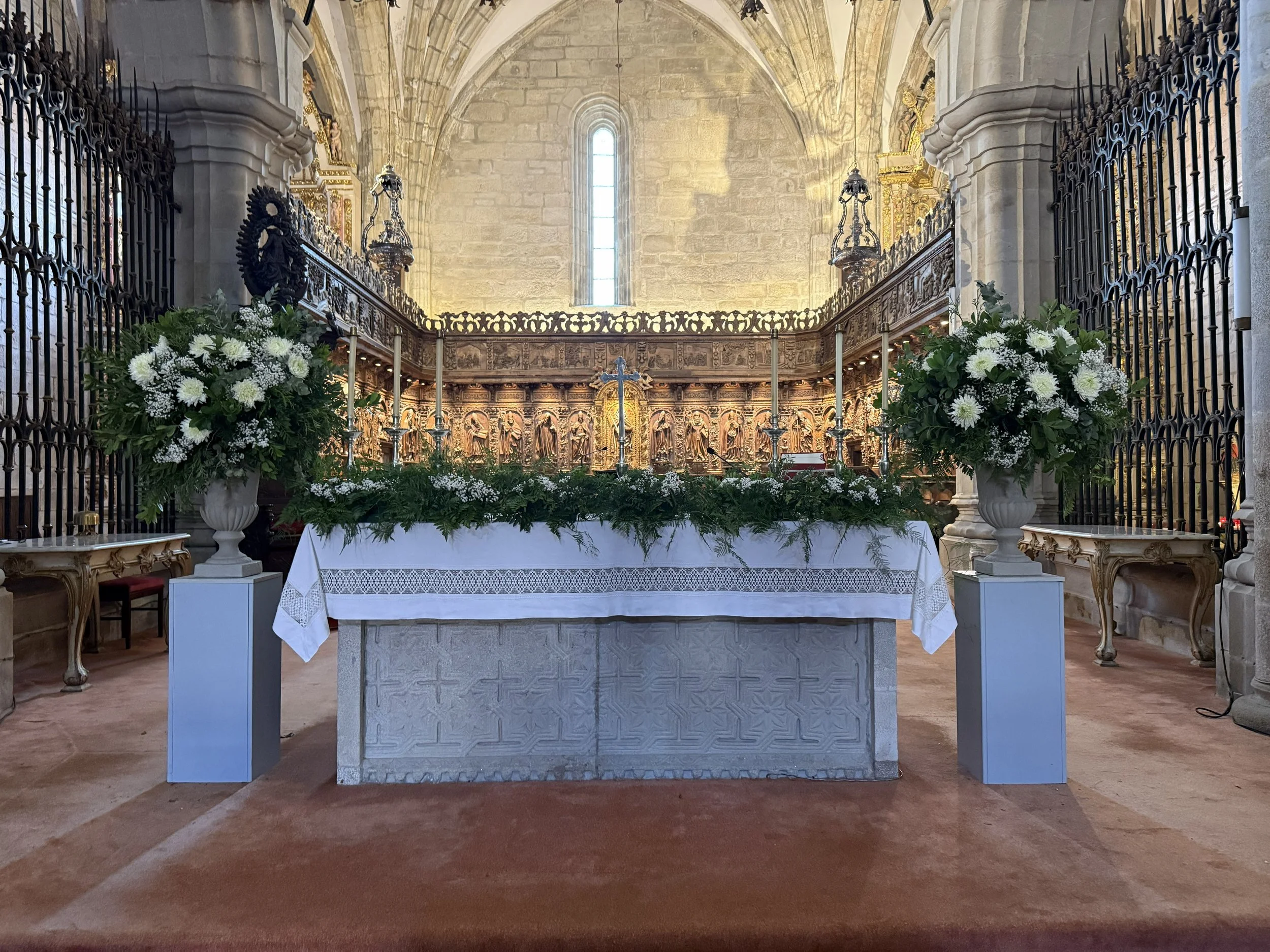 Interior de una iglesia con altar decorado con flores blancas, candelabros y detalles dorados.