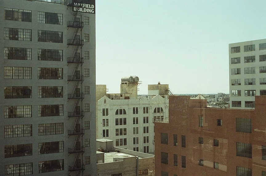 View of city buildings with various architectural styles under a clear sky, seen through a window.