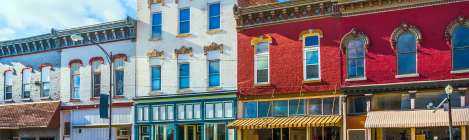 Colorful row of historic brick buildings with large windows and awnings on a city street.