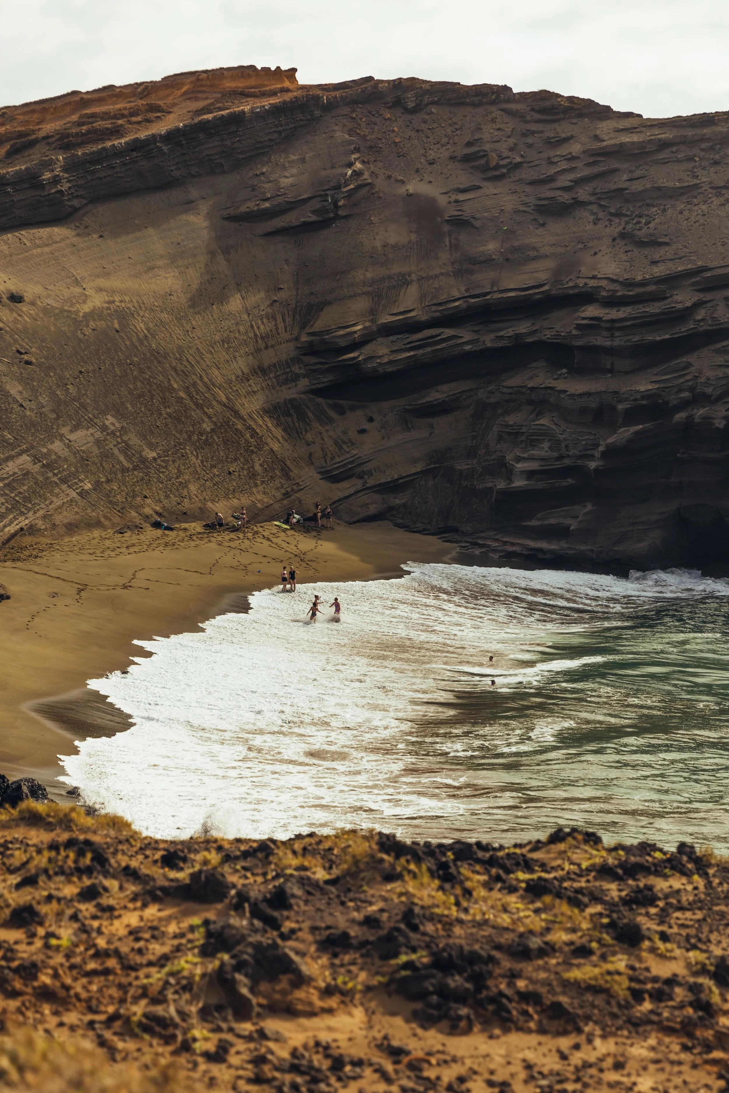 People on a beach with large rocky cliffs in the background