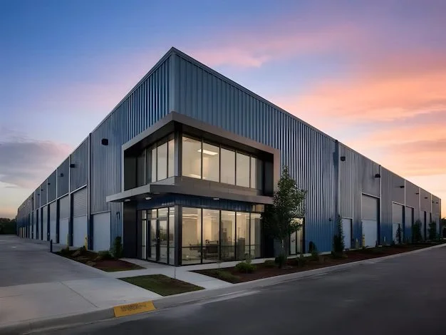 Modern industrial building with large glass windows and metal siding at sunset.
