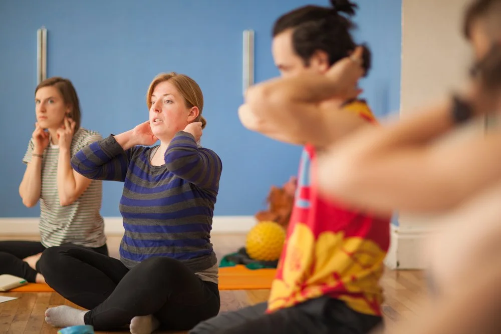 A group of people sitting on the floor participating in a relaxation or yoga session with a blue wall in the background.