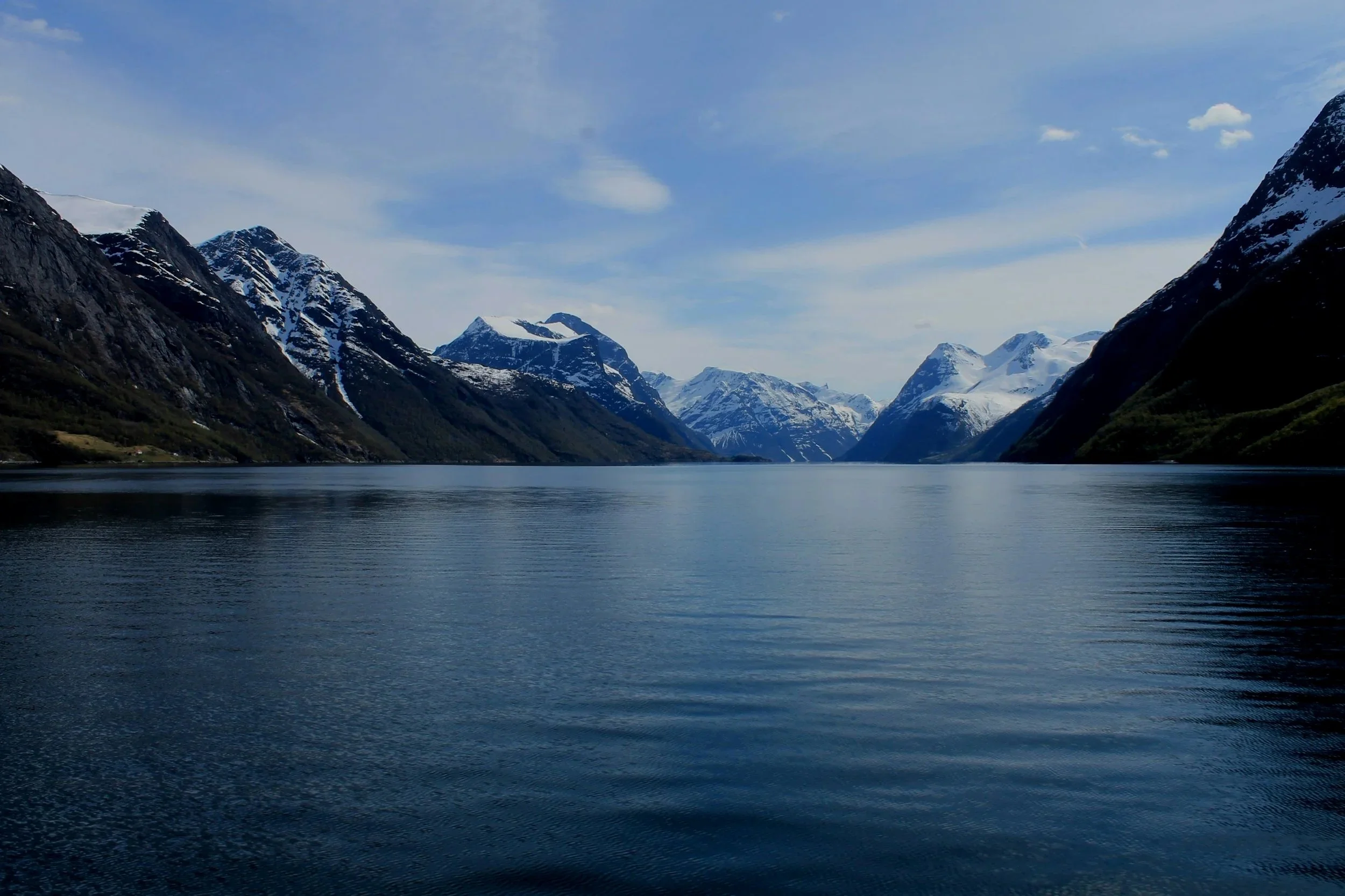 A scenic view of snow-capped mountains surrounding a calm body of water under a partly cloudy sky.