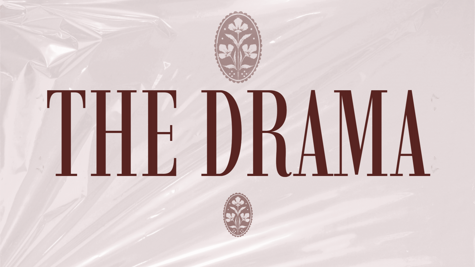 Packaging with the text 'The Drama' in large brown letters on a pink background, decorated with small floral emblems.