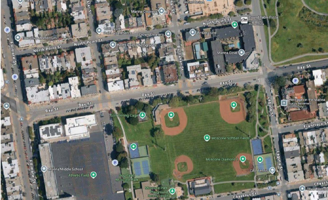 Satellite view of a neighborhood with a large park containing softball fields, playgrounds, tennis courts, and a golf driving cage, bordered by streets and residential buildings.