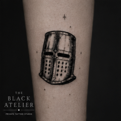 Tattoo of a metallic robot head on a person's arm, with a small star above it and text reading 'THE BLACK ATELIER PRIVATE TATTOO STUDIO' at the bottom.