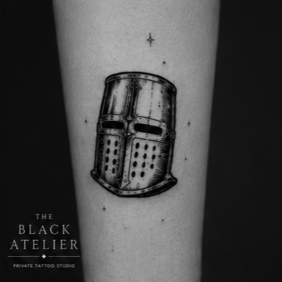 Black and gray tattoo of a helmet, with a small star above it, on forearm.
