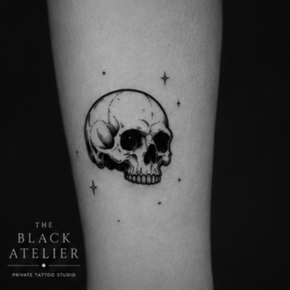 Tattoo of a skull with stars around it on skin, with text 'The Black Atelier Private Tattoo Studio' in the corner.