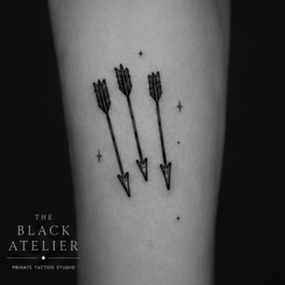 Tattoo of three black arrows pointing down, surrounded by small stars, on skin.