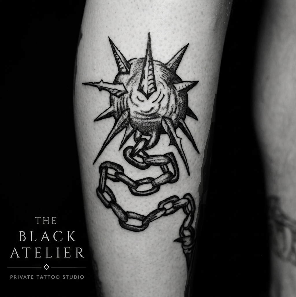 A black and white tattoo of a medieval flail weapon, on light skin.