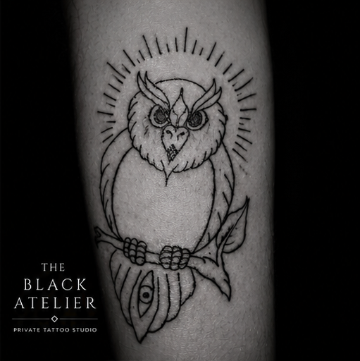 Black and white tattoo of an owl with a halo of lines around its head, perched on a branch with a leaf, detailed with intricate line work.