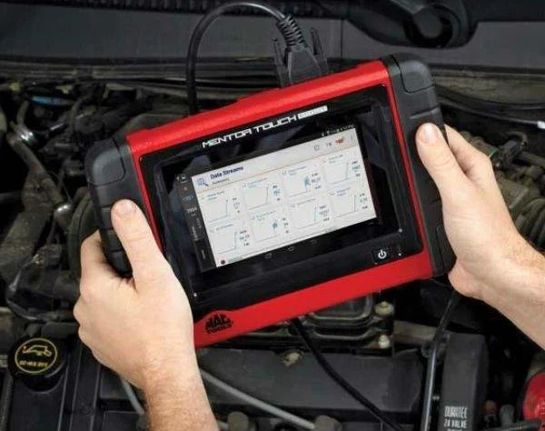 Person holding a red diagnostic scan tool connected to a car engine.