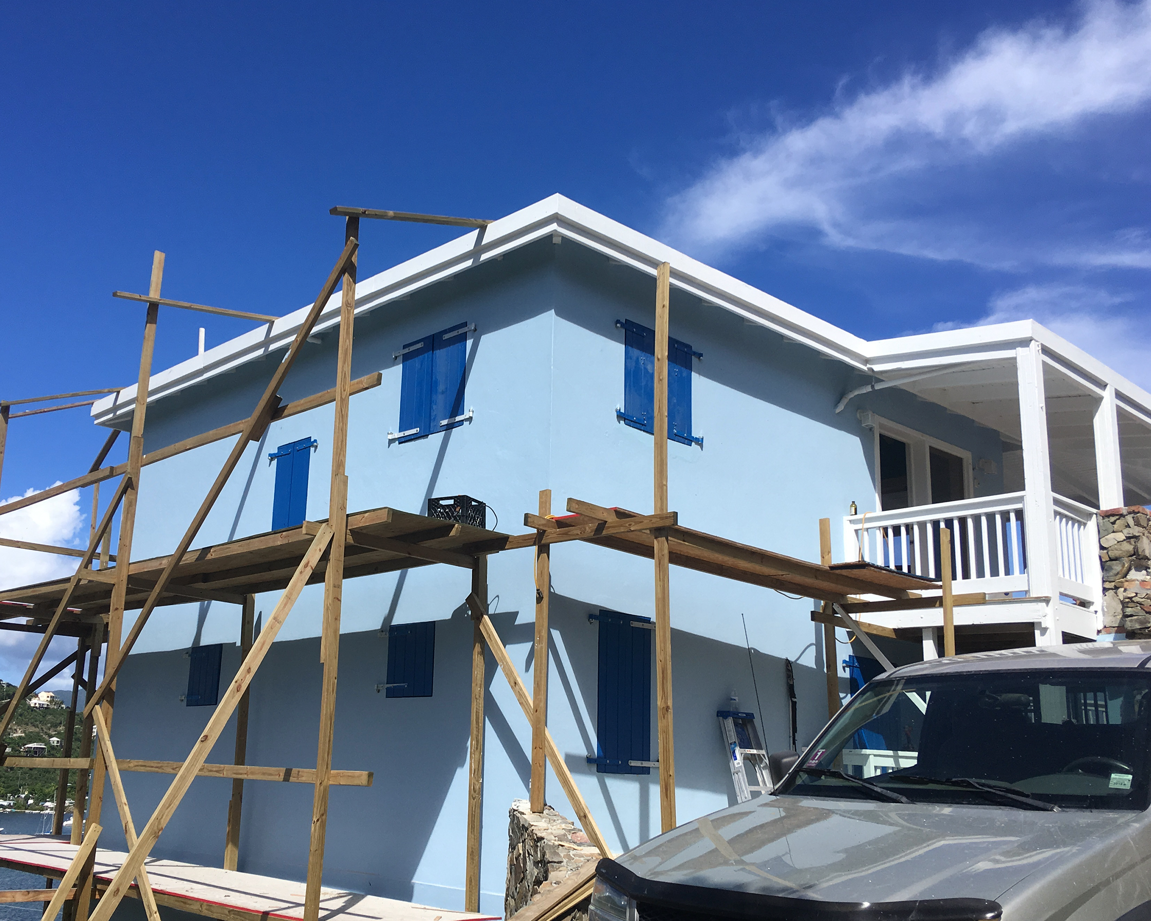 The light blue Coral Bay house under construction with scaffolding around it, and blue shutters on the windows, against a blue sky with a few clouds.