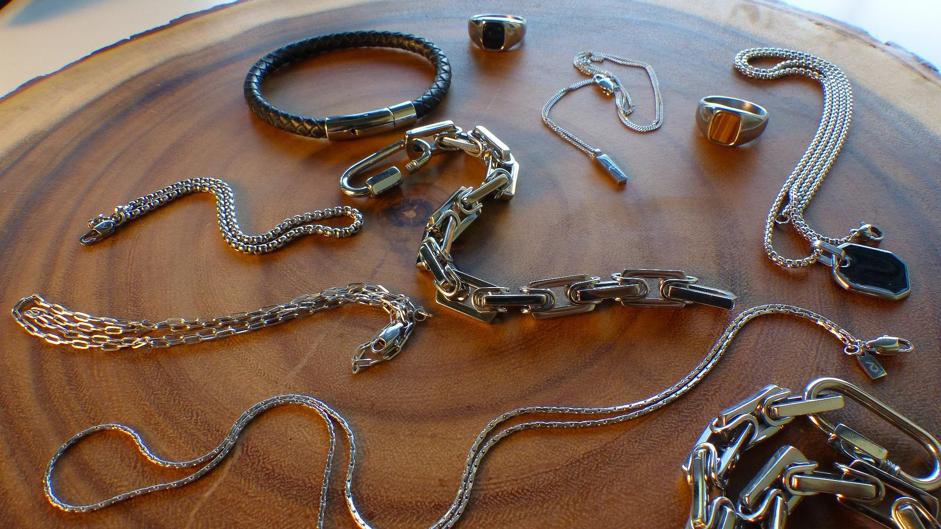 Various silver and gold jewelry pieces including necklaces, chains, rings, and bracelets displayed on a round wooden surface.