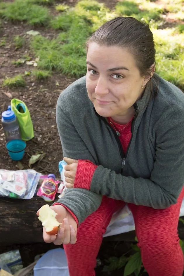 Dr. Katie during a backpacking trip to soothe her mental health, sitting outdoors on a log surrounded by camping gear.