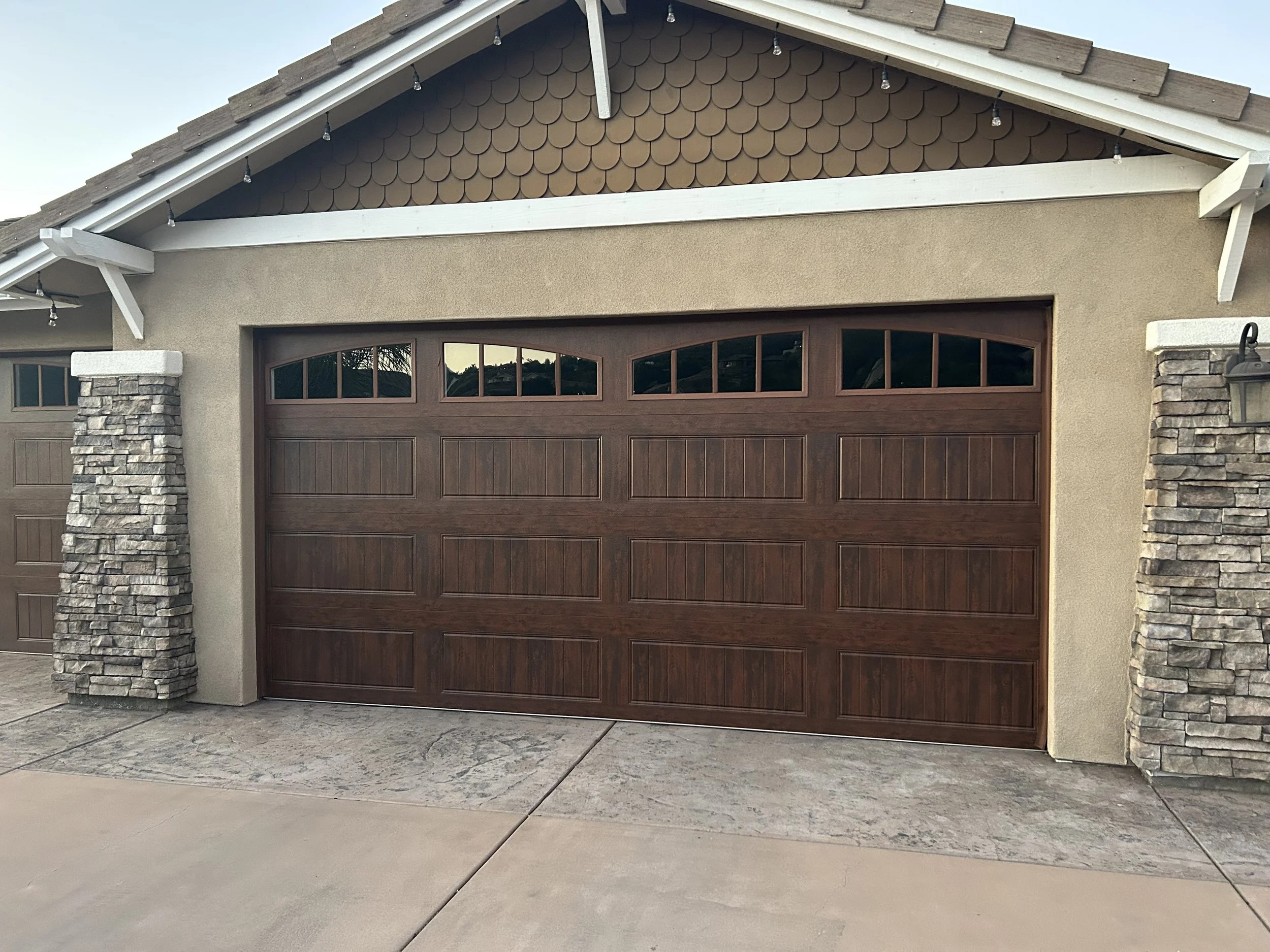 Custom wood-look residential garage door with arched windows installed by Alpine Overhead Doors in San Diego County.