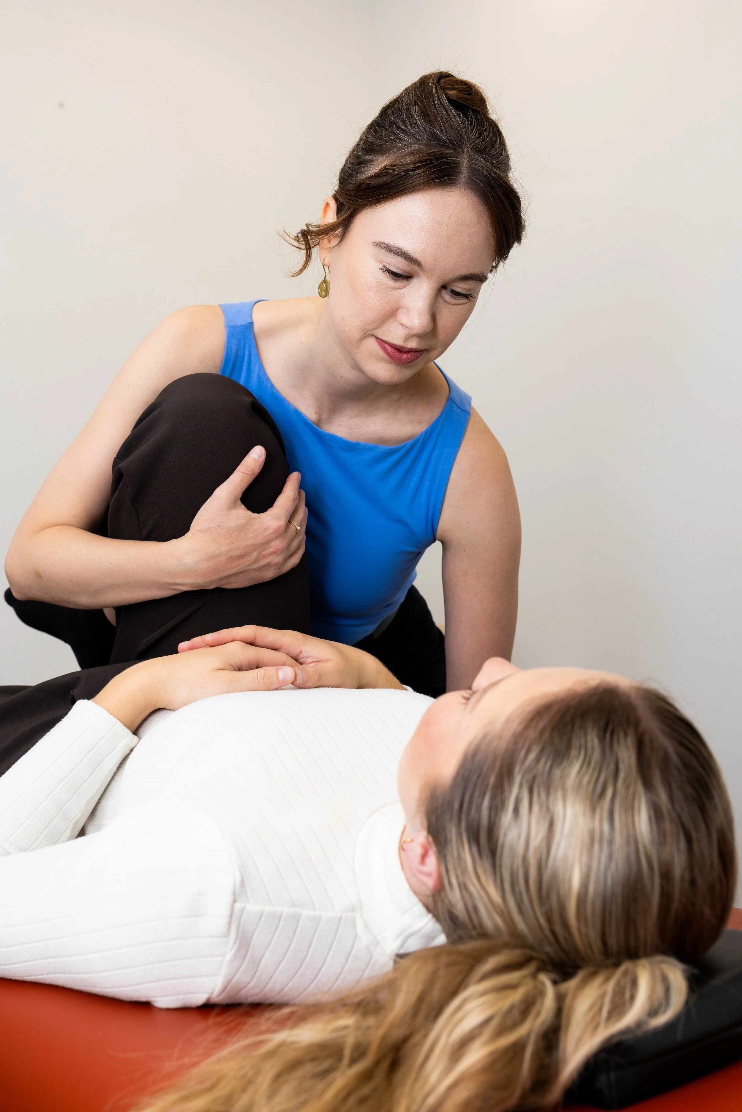 A woman is performing an osteopathic technical application whereby she is moving the patient’s bent leg. The patient is lying on her back on a treatment table.