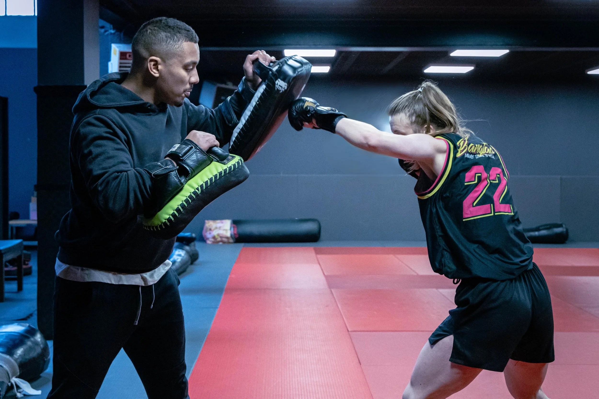 Deux personnes s'entraînent dans à la boxe et au mma, la fille pratique la boxe ou le Muay Thai avec un coup vers le pao maintenu par un entraîneur.