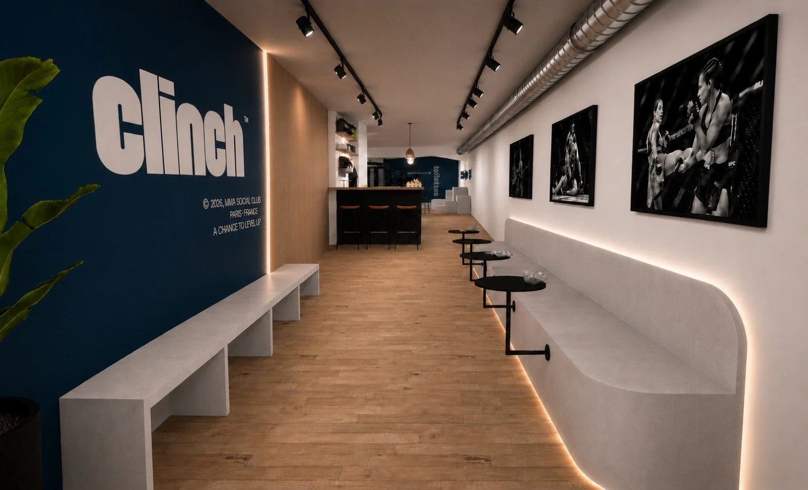 Intérieur d'un espace moderne avec un mur bleu avec le logo 'clinch' et un plan de travail, une banquette blanche le long du mur avec des petites tables, des cadres noirs avec des photos de femmes boxeuses, et un sol en bois.