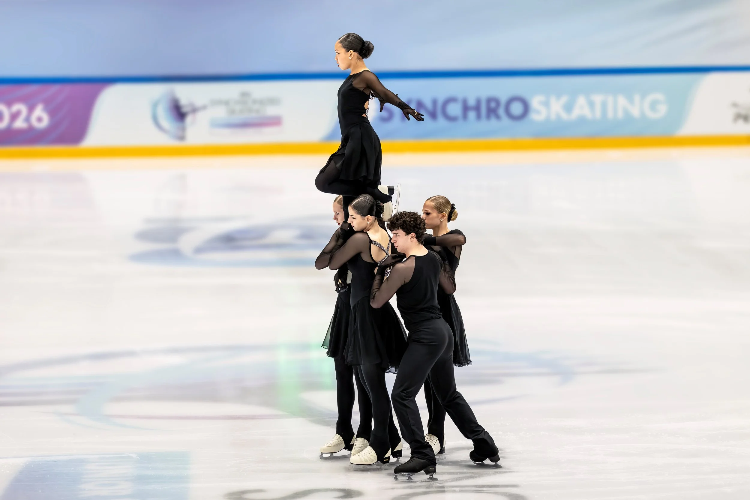 A group of five female figure skaters performing a synchronized routine on the ice rink during a competition.