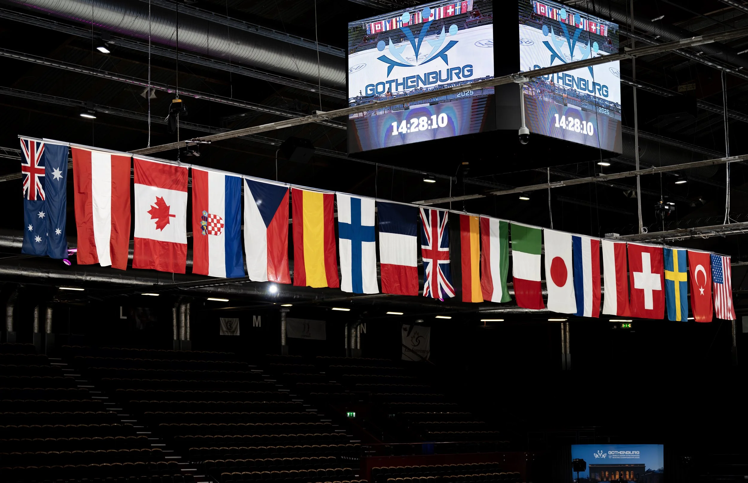 Flags of various countries hanging inside a sports arena, with a digital scoreboard displaying the logo for Gothenburg and a countdown timer.
