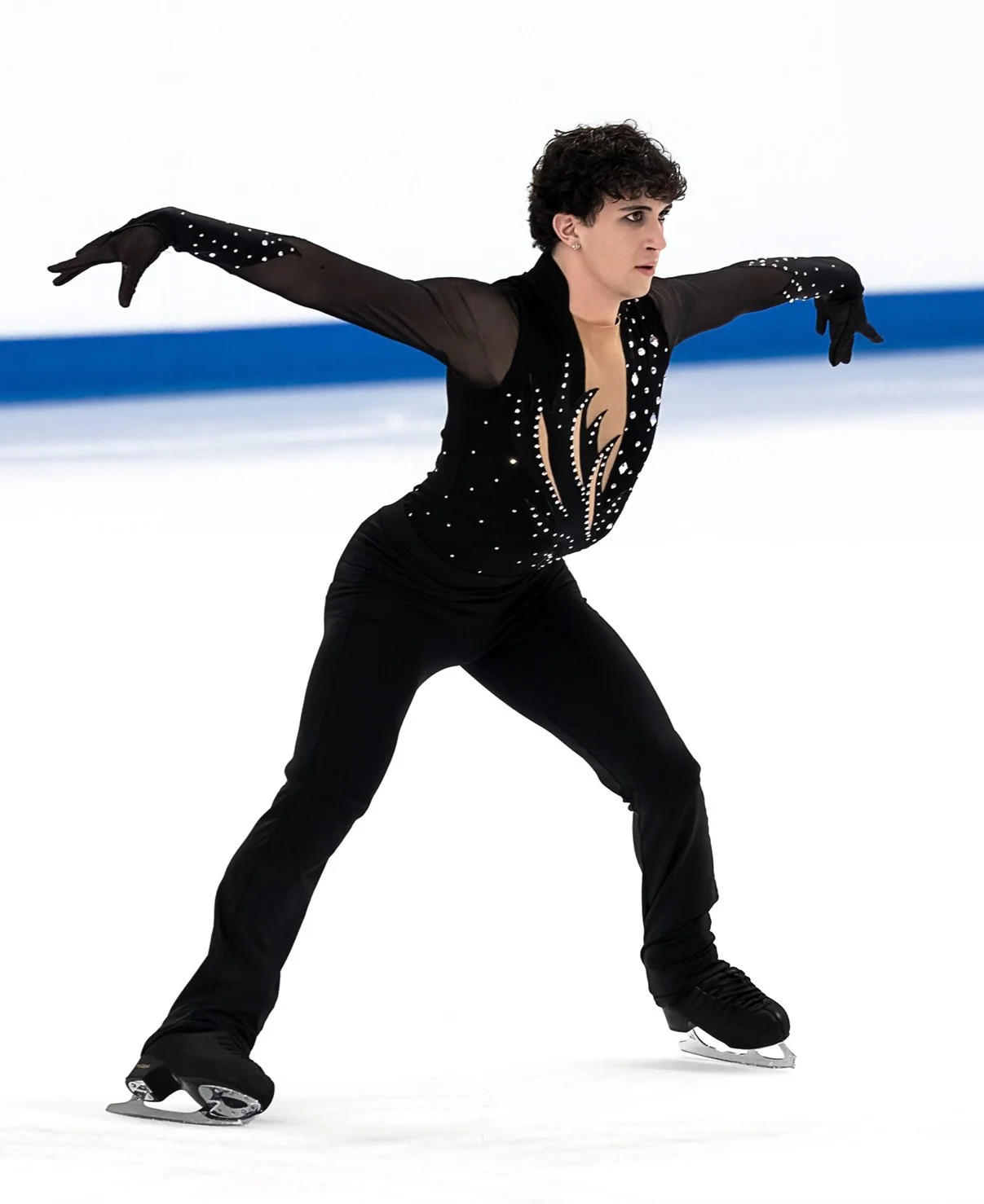 A figure skater performing on ice, dressed in a black costume with silver and rhinestone embellishments.