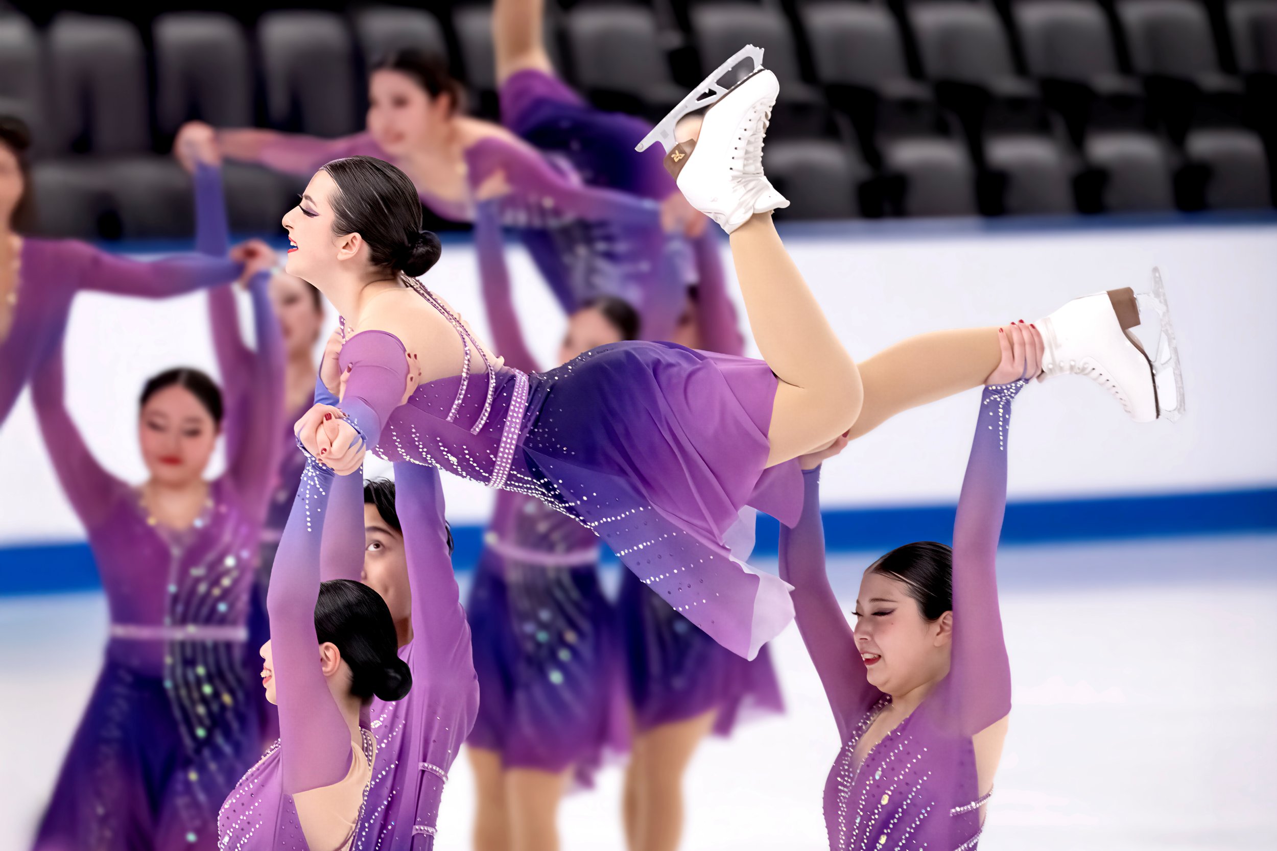 A group of female figure skaters in purple costumes practicing synchronized moves on ice, one skater being lifted by others.