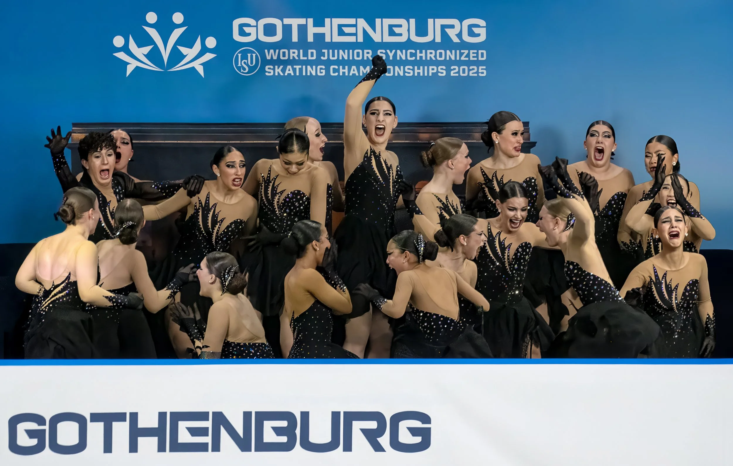 A group of figure skaters wearing black and tan costumes performing at the World Junior Synchronized Skating Championships 2025 in Gothenburg, with a blue background and the event's logo.