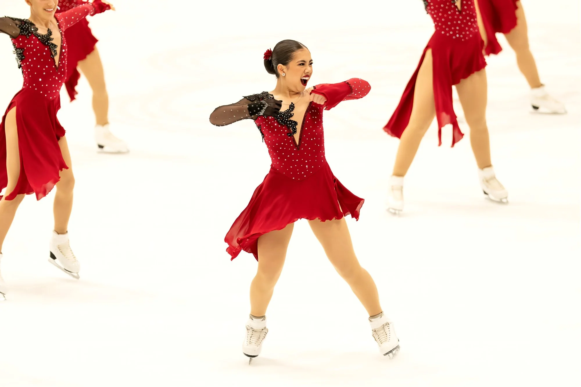 A group of figure skaters performing a routine on ice, dressed in red costumes with black and sparkling details.