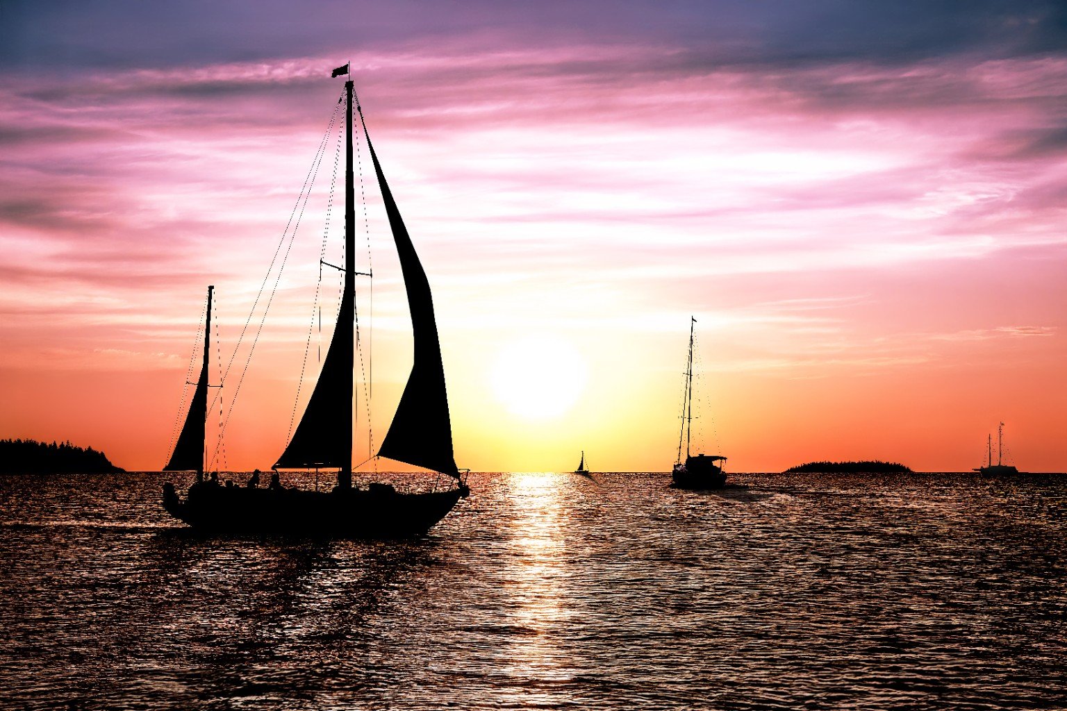 Silhouettes of sailboats on water during a colorful sunset with pink, purple, and orange sky.
