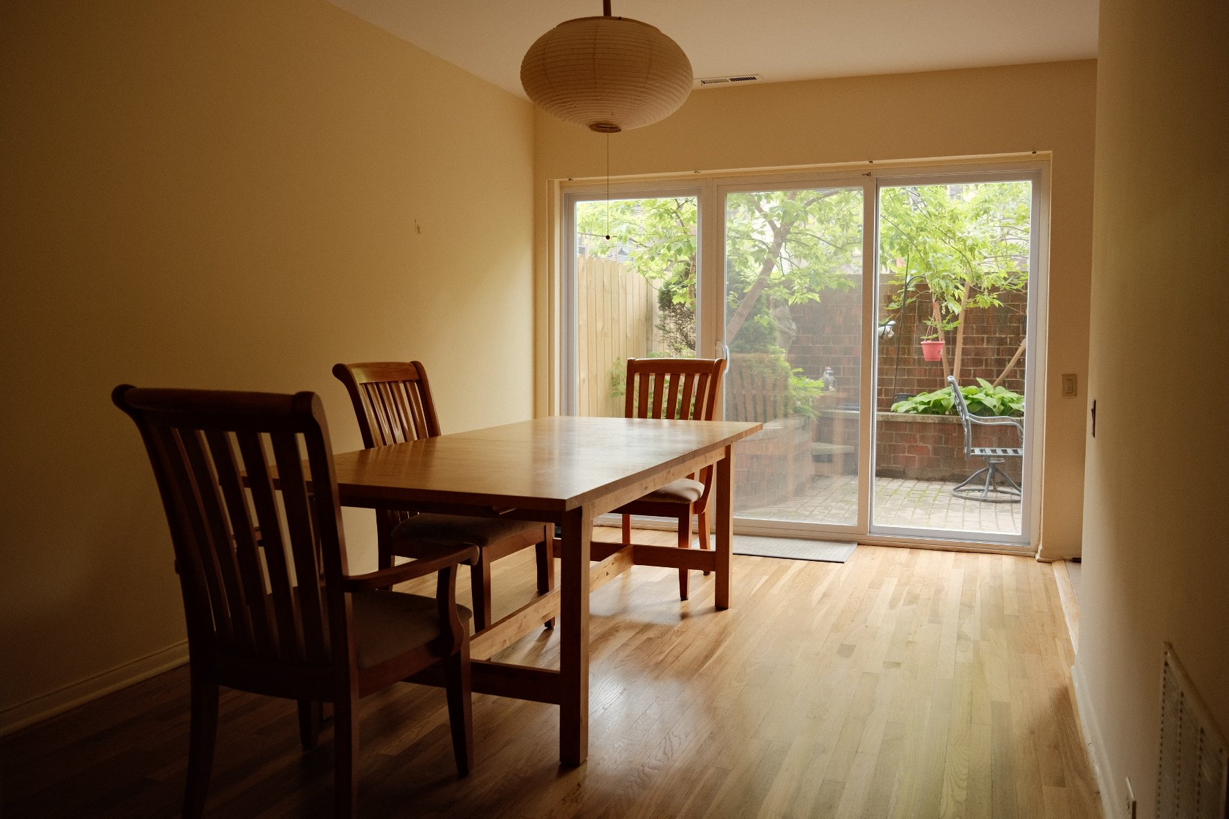 Dining room in Hyde Park townhome with a wooden table and three chairs, sliding glass door leading to a patio with outdoor furniture and greenery.