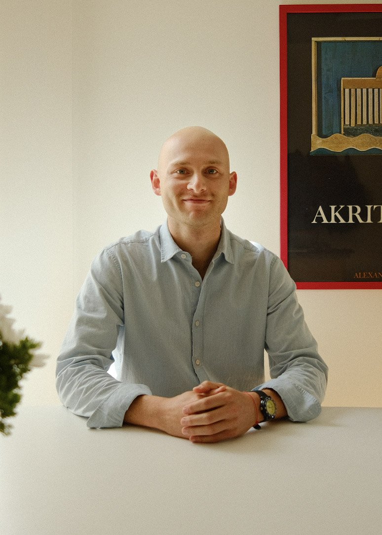 A smiling bald man, Jeremy Padorr who is a Realtor® in Chicago. He is in a light blue button-up shirt sitting at a white table with hands folded, in an office or conference room, with a framed art piece on the wall behind him.