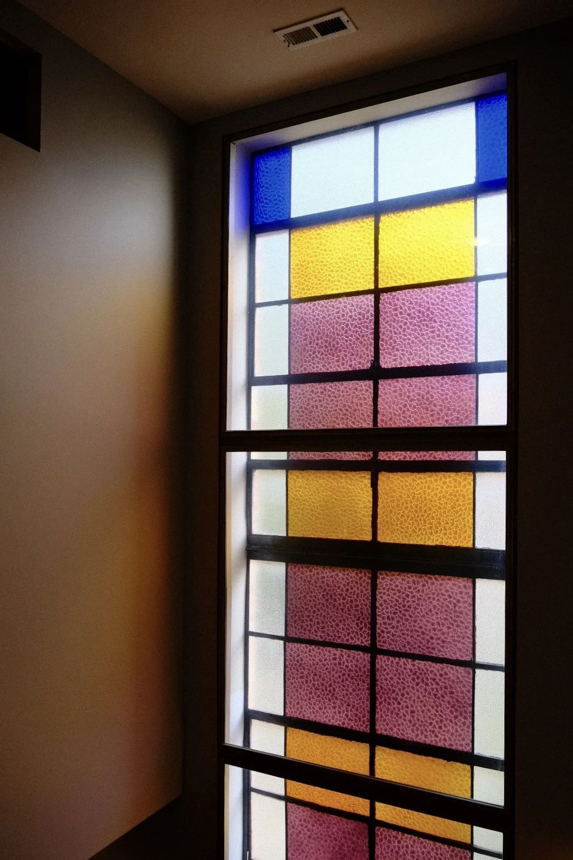 Colorful stained glass window in Old Town Chicago with blue, yellow, pink, and white sections, framed by black borders, located in an indoor setting.