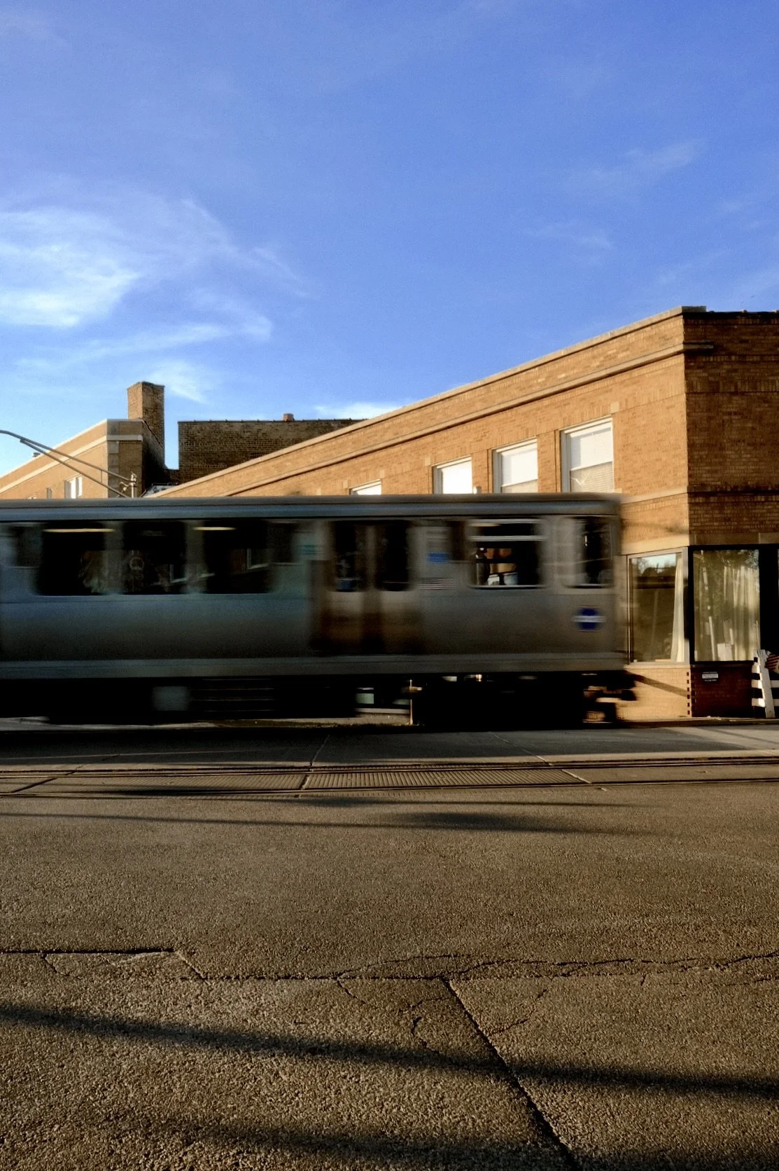 A moving train passing by on the tracks in front of a brick building in Ravenswood Manor Chicago with multiple windows and a blue sky overhead.