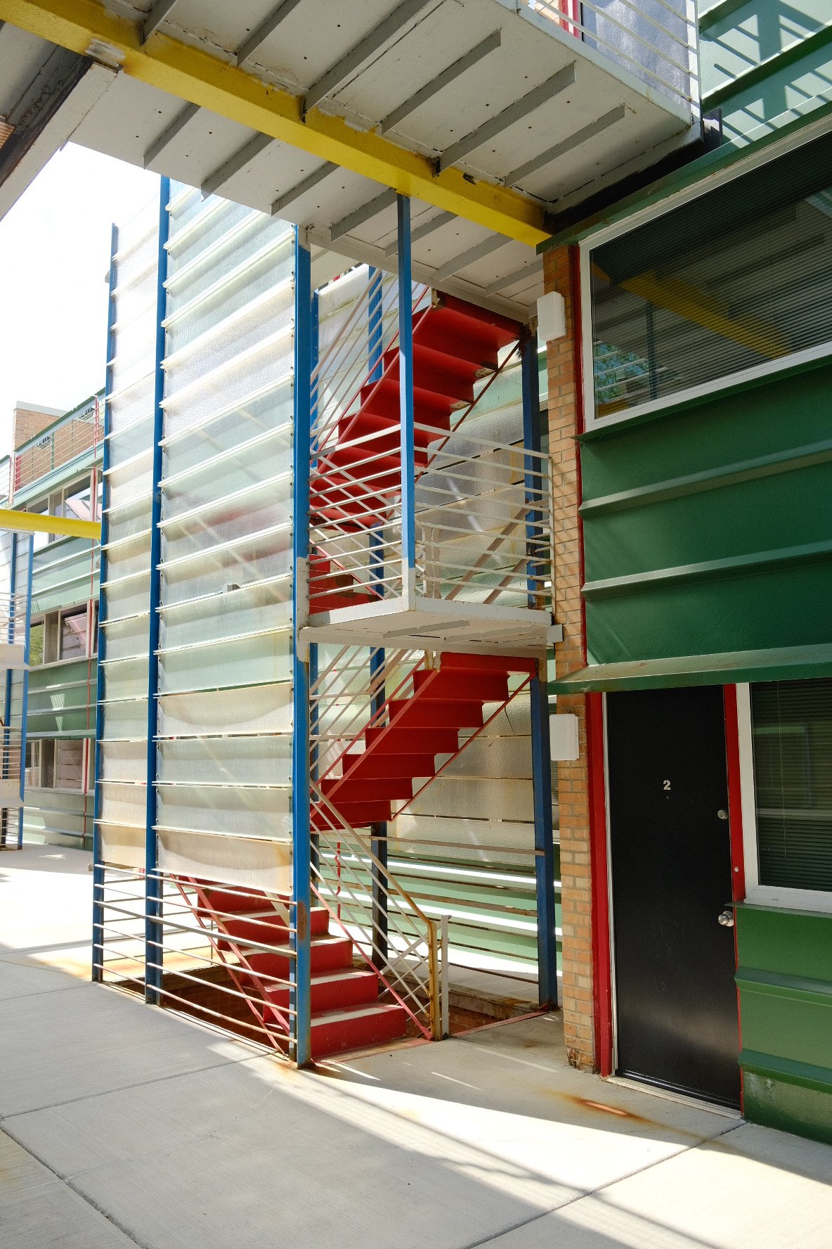 Exterior view of a colorful apartment building in Evanston with a red outdoor staircase and green and white window shutters.