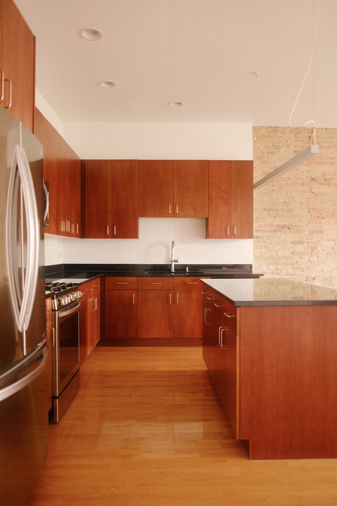 Modern kitchen in Wicker Park Chicago with wooden cabinets, black countertops, stainless steel appliances, and a brick accent wall.