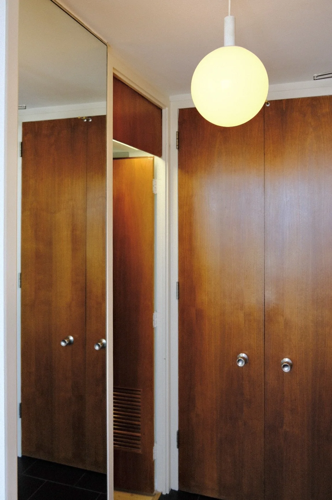 Interior view of entry hallway in Gold Coast condo with wooden cabinets and a round hanging light fixture.