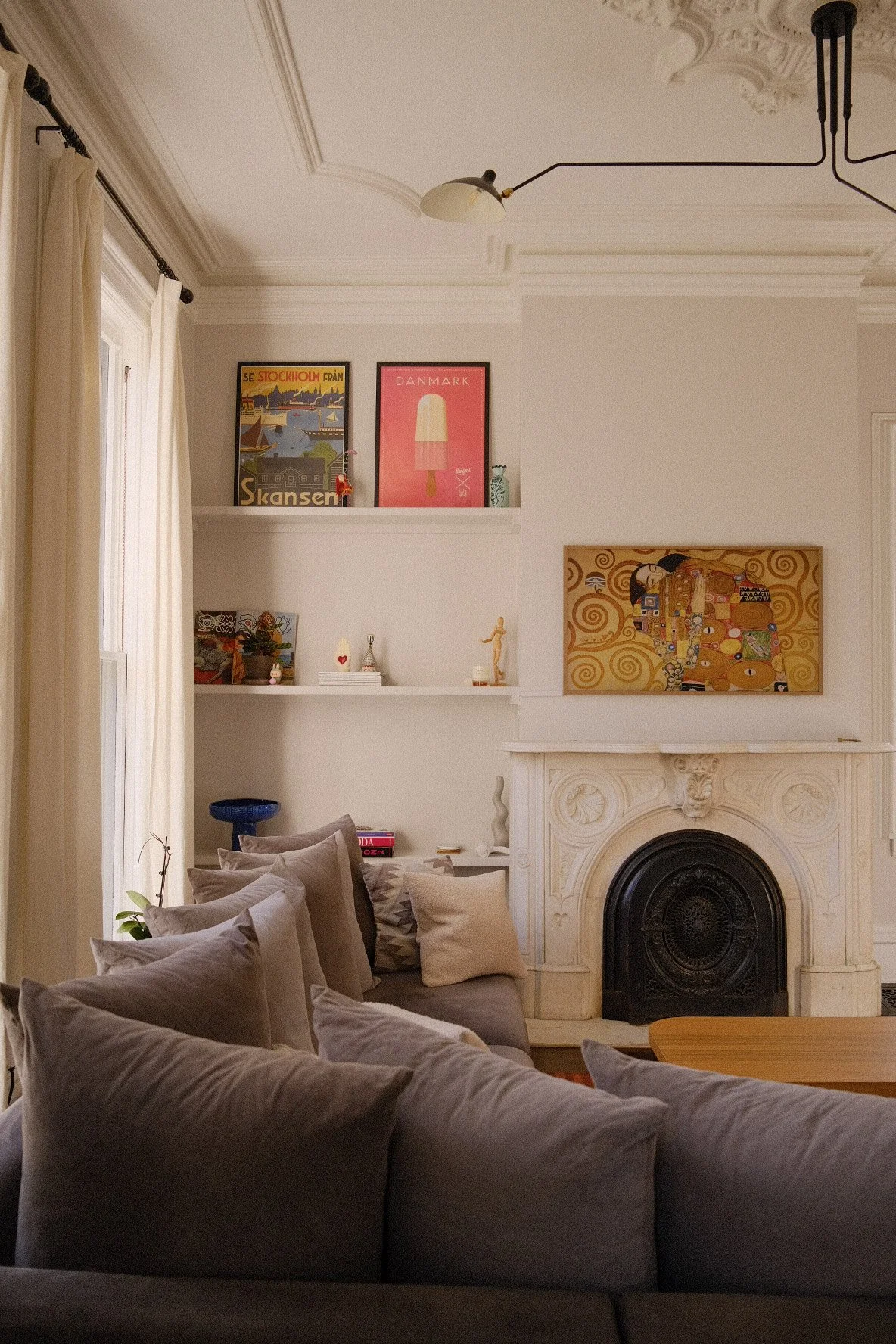 Living room in Evanston with a white ornate fireplace, framed artwork, shelves with decorative items, a cozy sectional sofa with pillows, and soft natural lighting from window curtains.