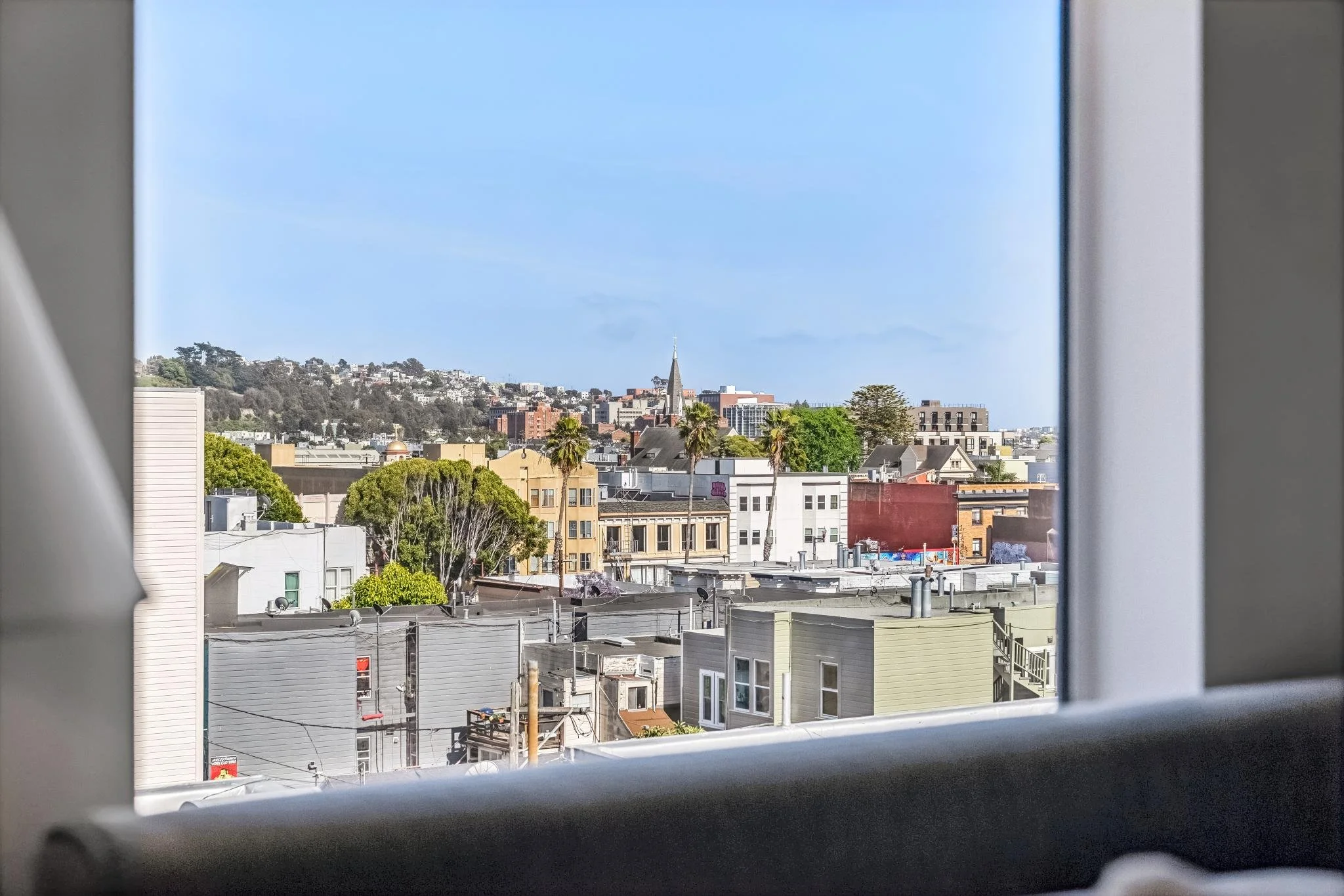 Cityscape view of buildings, trees, and a church steeple seen through a window frame.