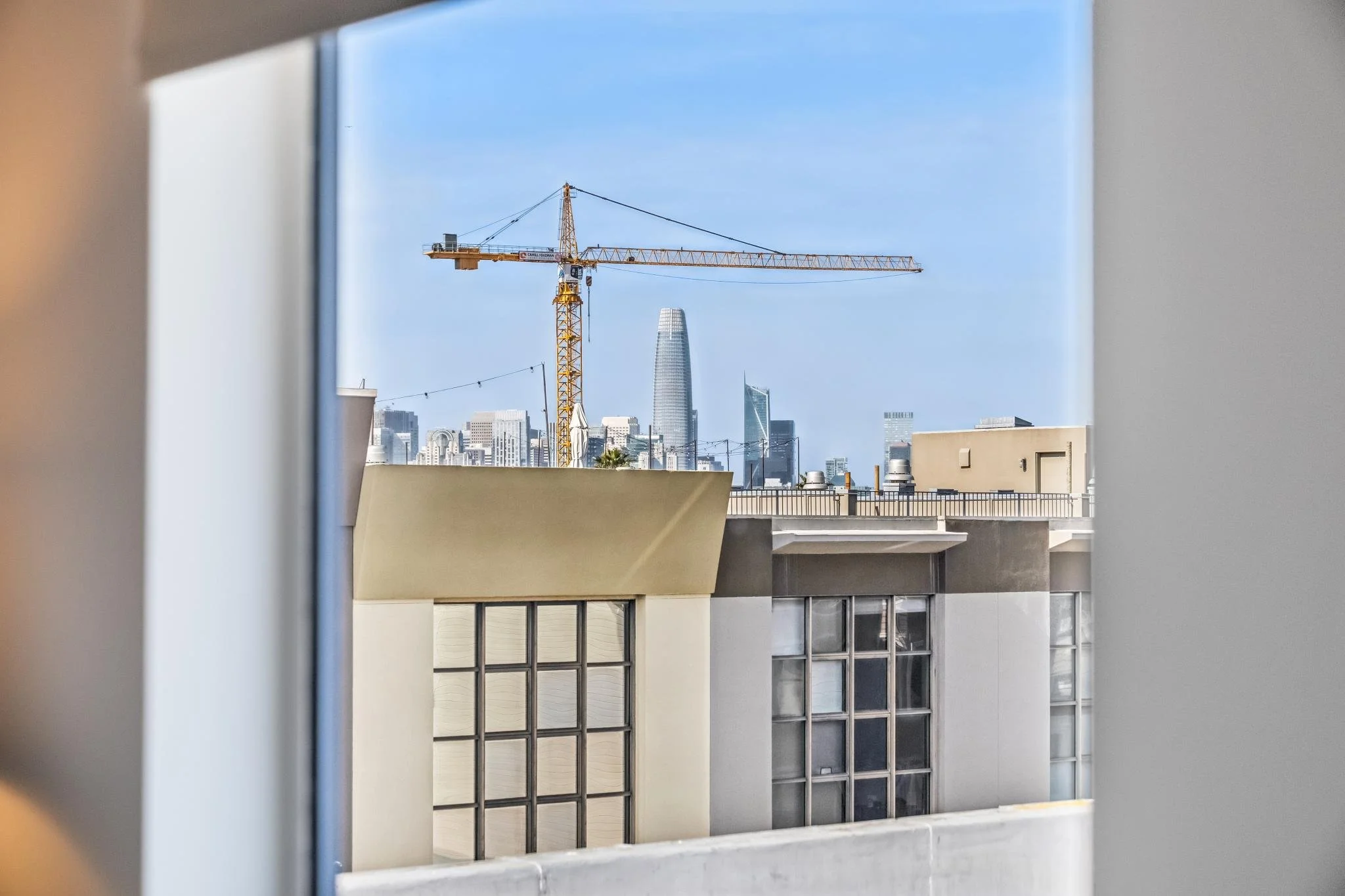 View of a city skyline with a yellow crane in the foreground, and several modern tall buildings, including the Salesforce Tower, under a blue sky.