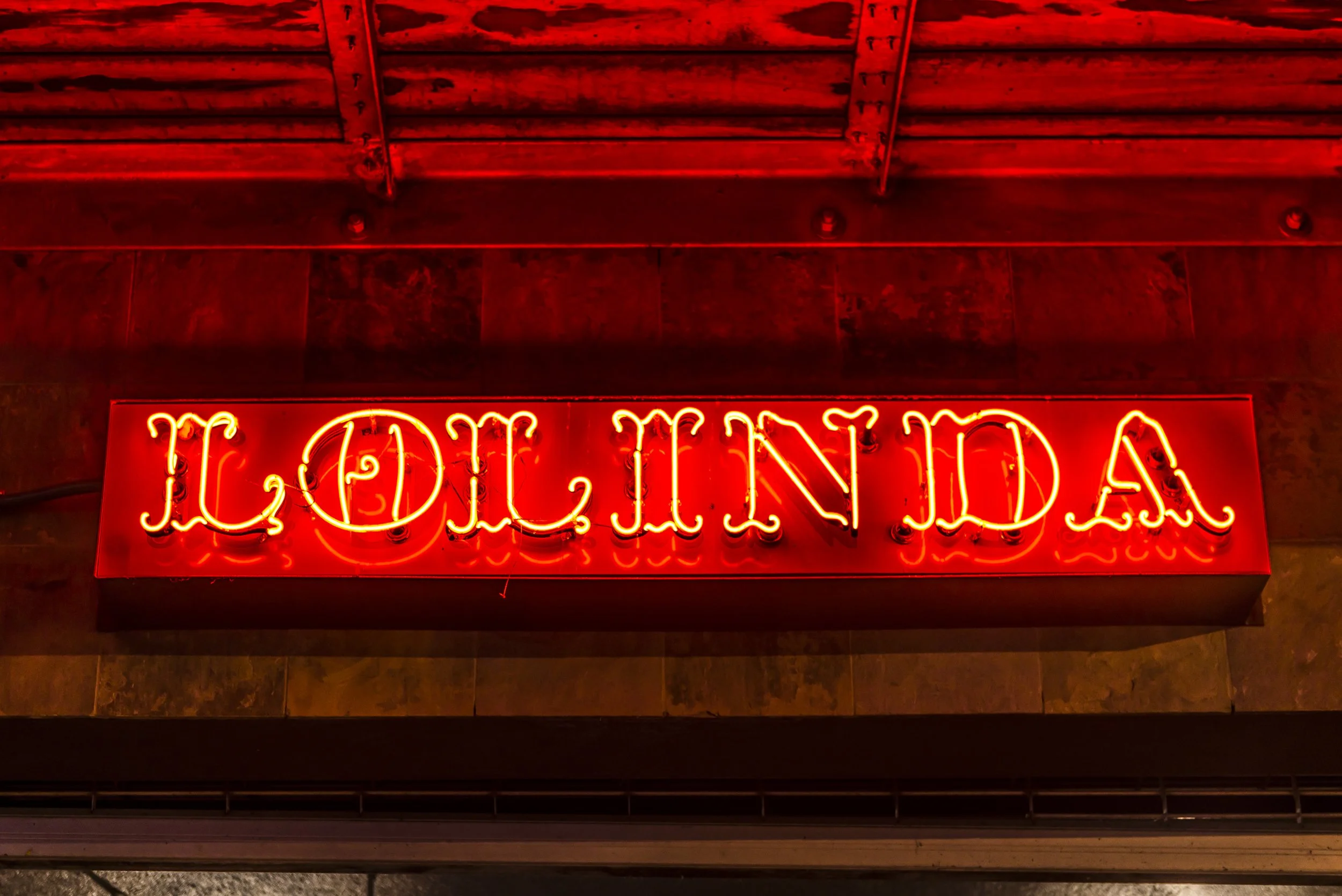 Bright red neon sign with cursive text reading 'Liquid Lounge' mounted on a dark wall, partially visible at the bottom of the image.