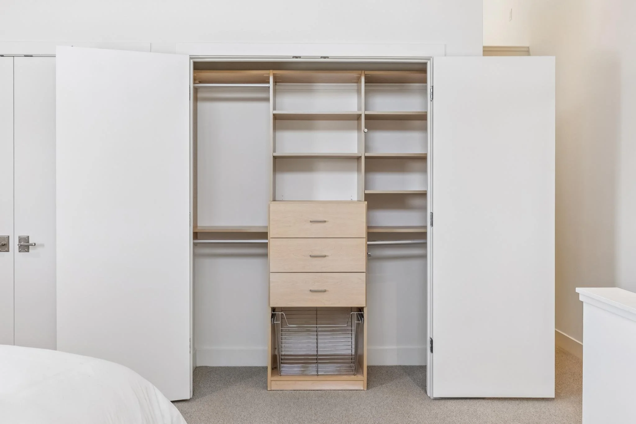 View of an empty closet with white double doors open, revealing internal shelves and drawers in a neoclassical style bedroom.