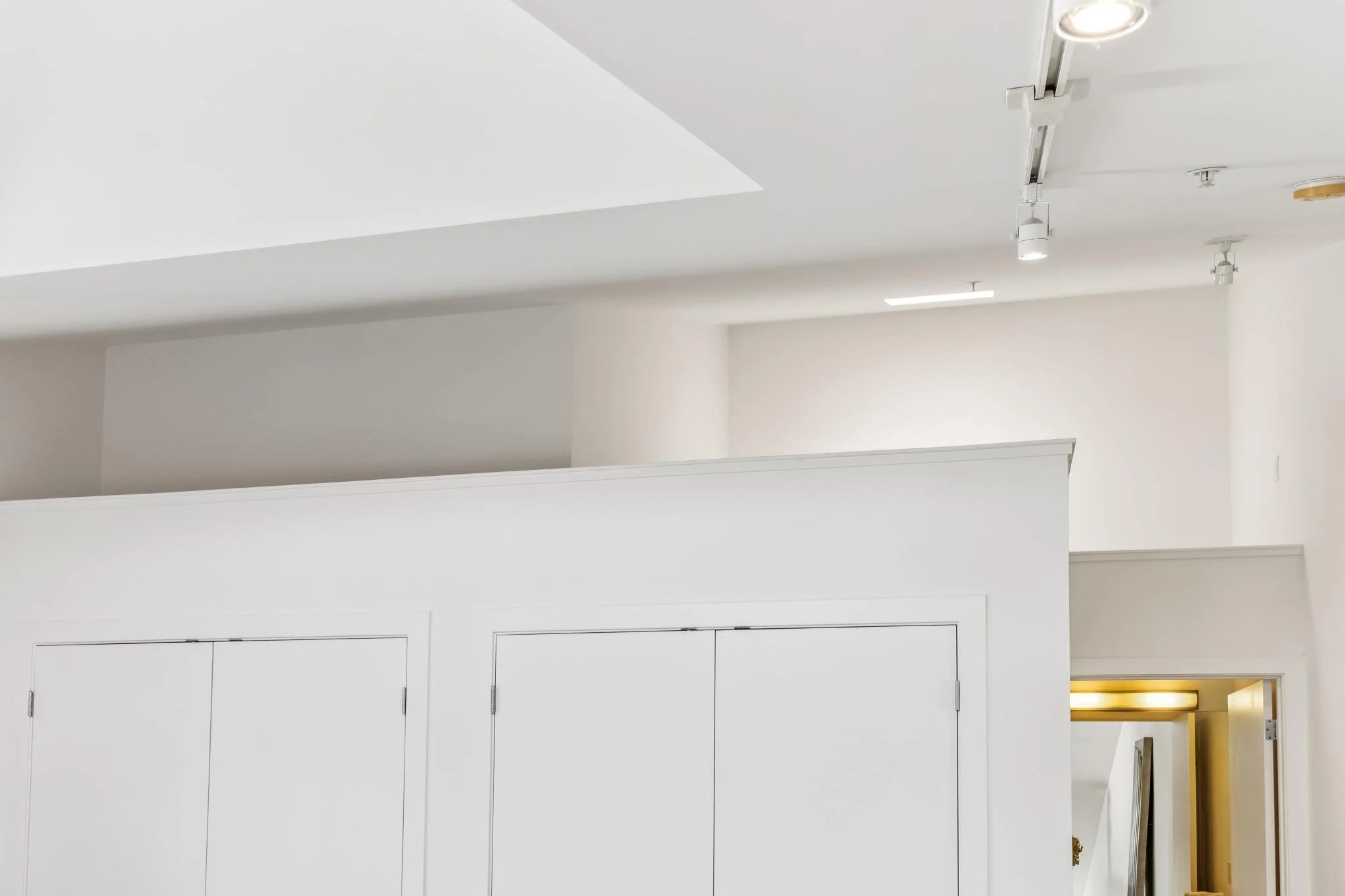 Interior view of a modern white office or commercial space with ceiling lights, a skylight, and a section of yellow wall visible in the background.