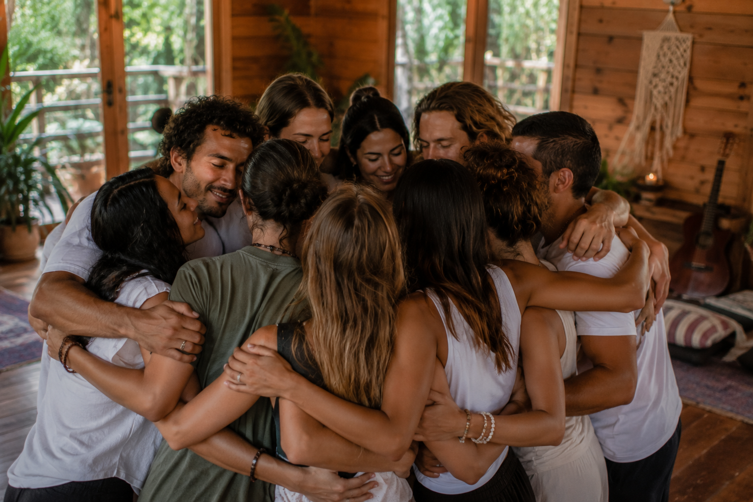 Grupo de personas abrazándose en una reunión cálida en un ambiente de madera con ventanas grandes y plantas.