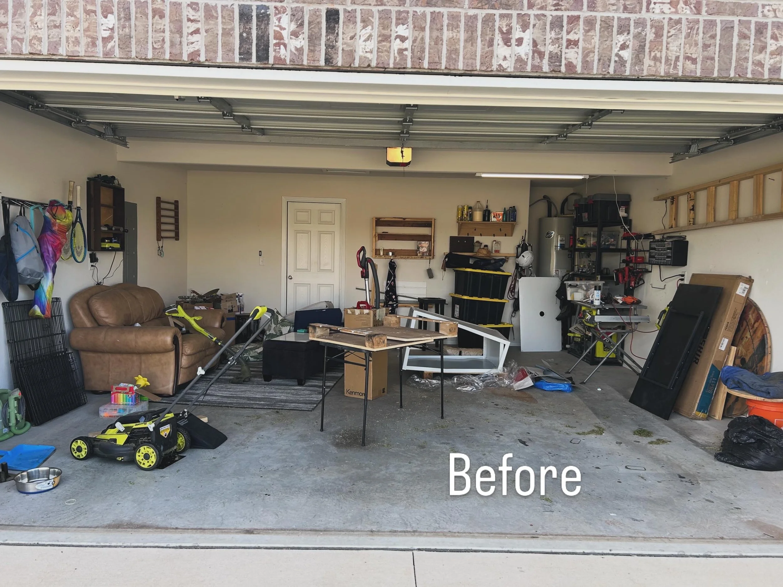 Garage filled with various items including a brown leather couch, a yellow and black toy car, a foldable table, shelves with tools, boxes, bags, and other miscellaneous objects.
