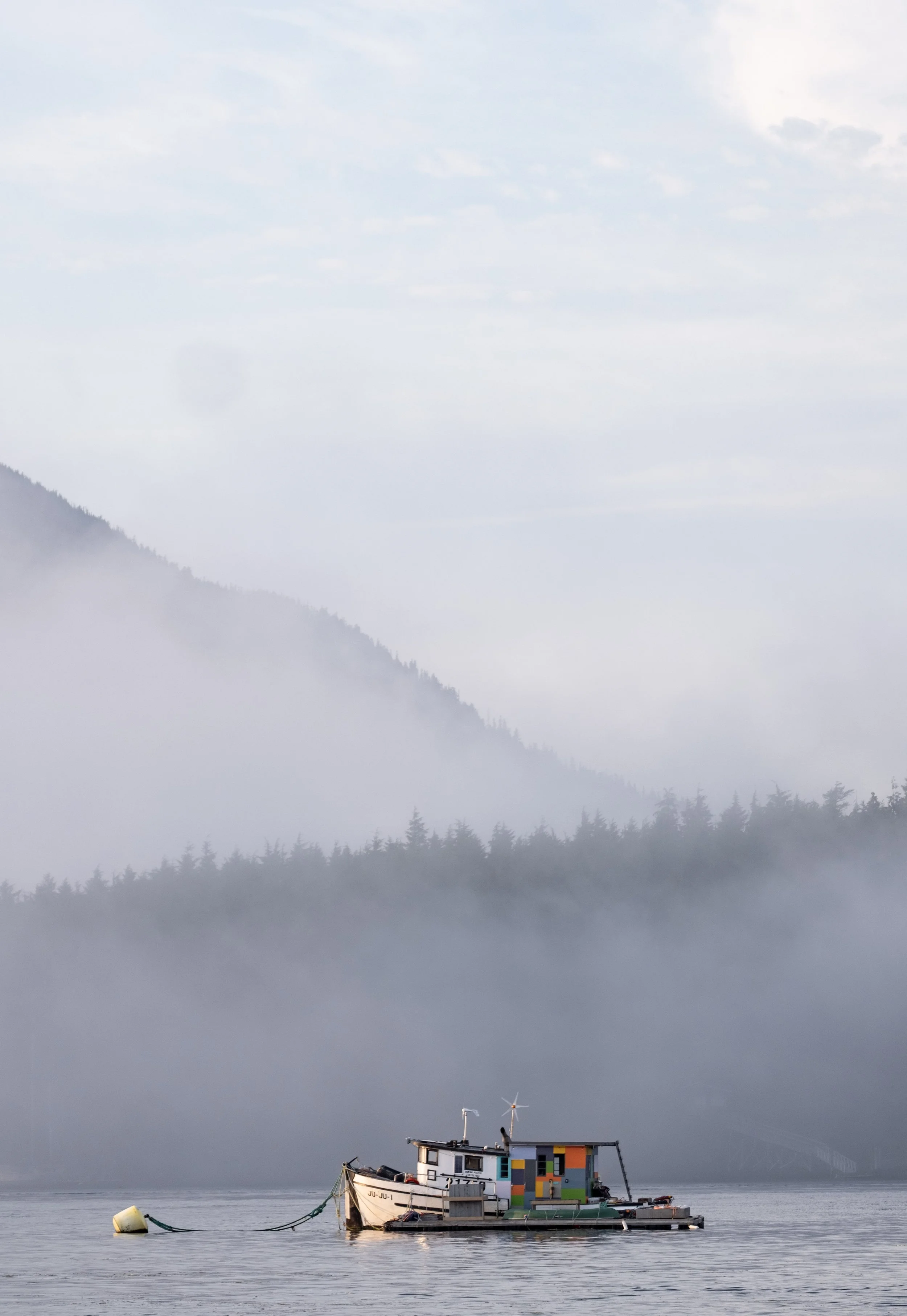 A colorful houseboat floating on calm water with mountains and mist in the background.