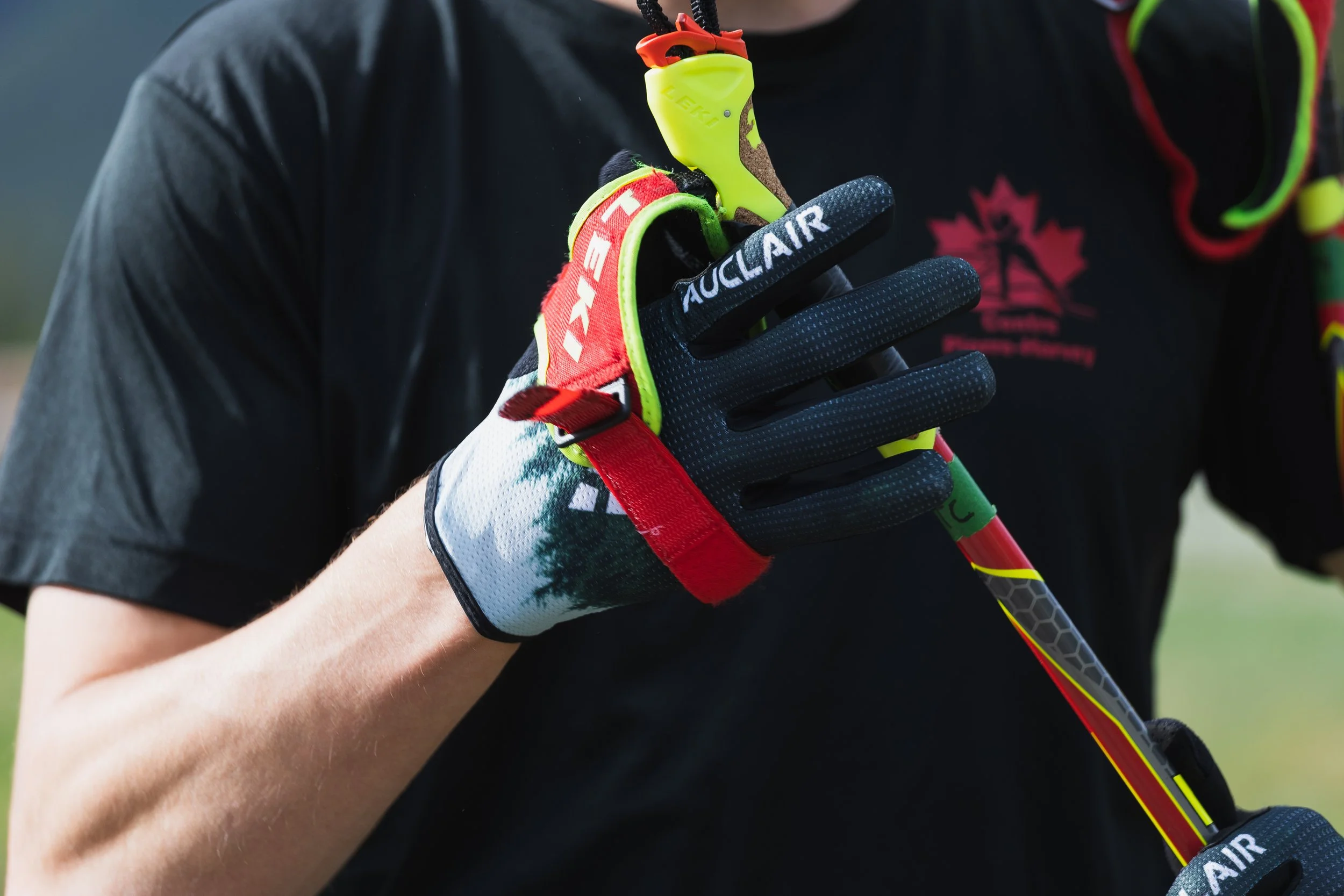 Close-up of a person wearing sports gloves holding a ski pole, with a focus on the gloves and ski pole, and part of a jacket with a Canadian maple leaf logo.