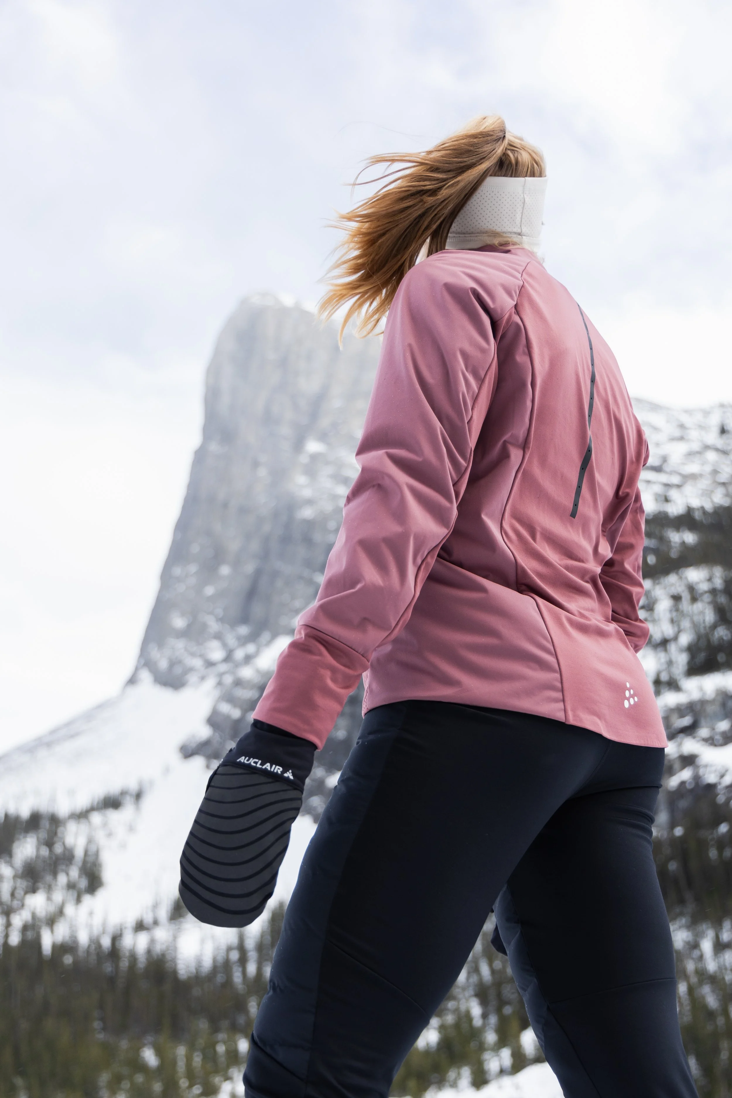 Person wearing a pink winter jacket and black pants skiing in a snowy mountain landscape.
