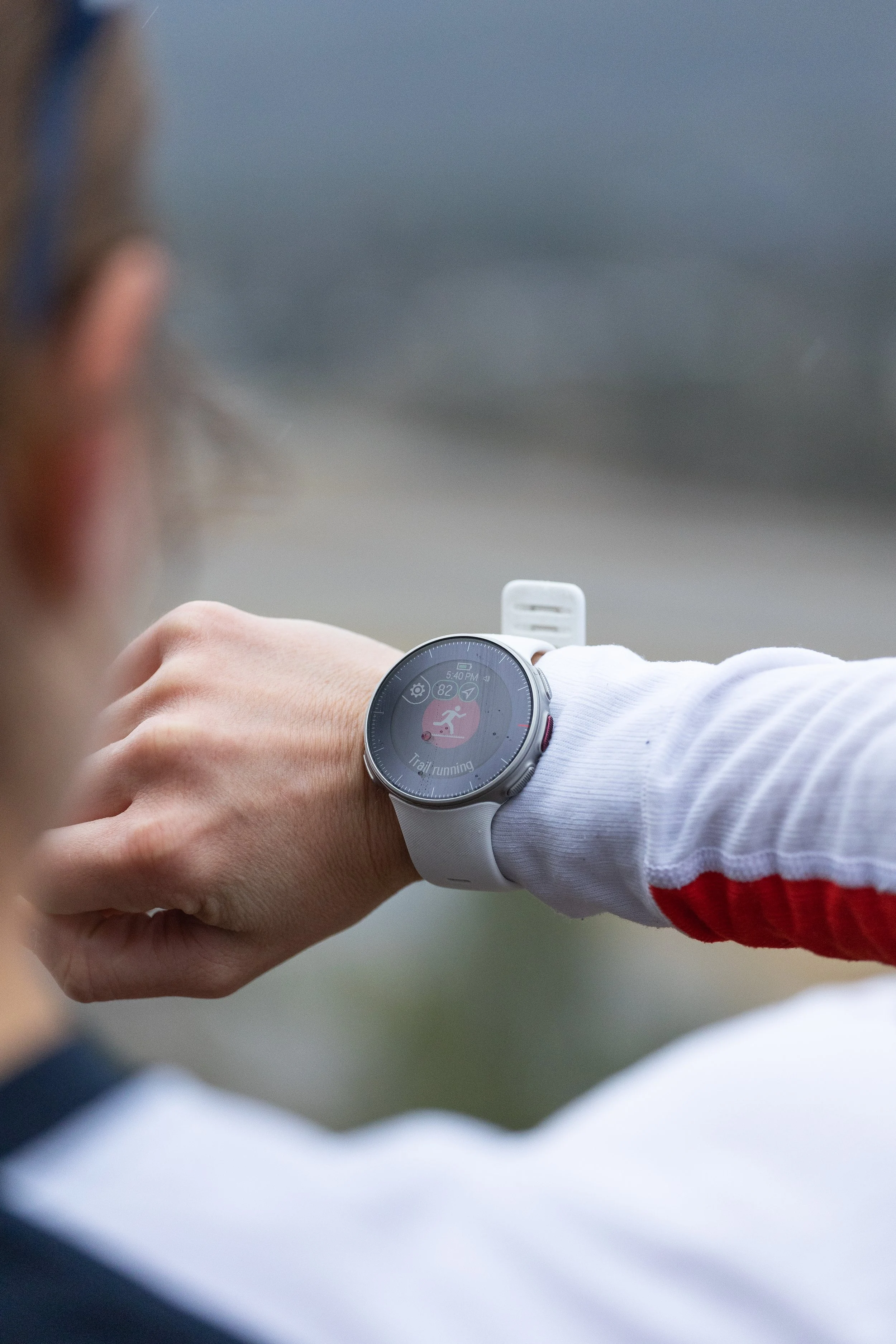 Person checking the time on a smartwatch while wearing a white and red jacket.