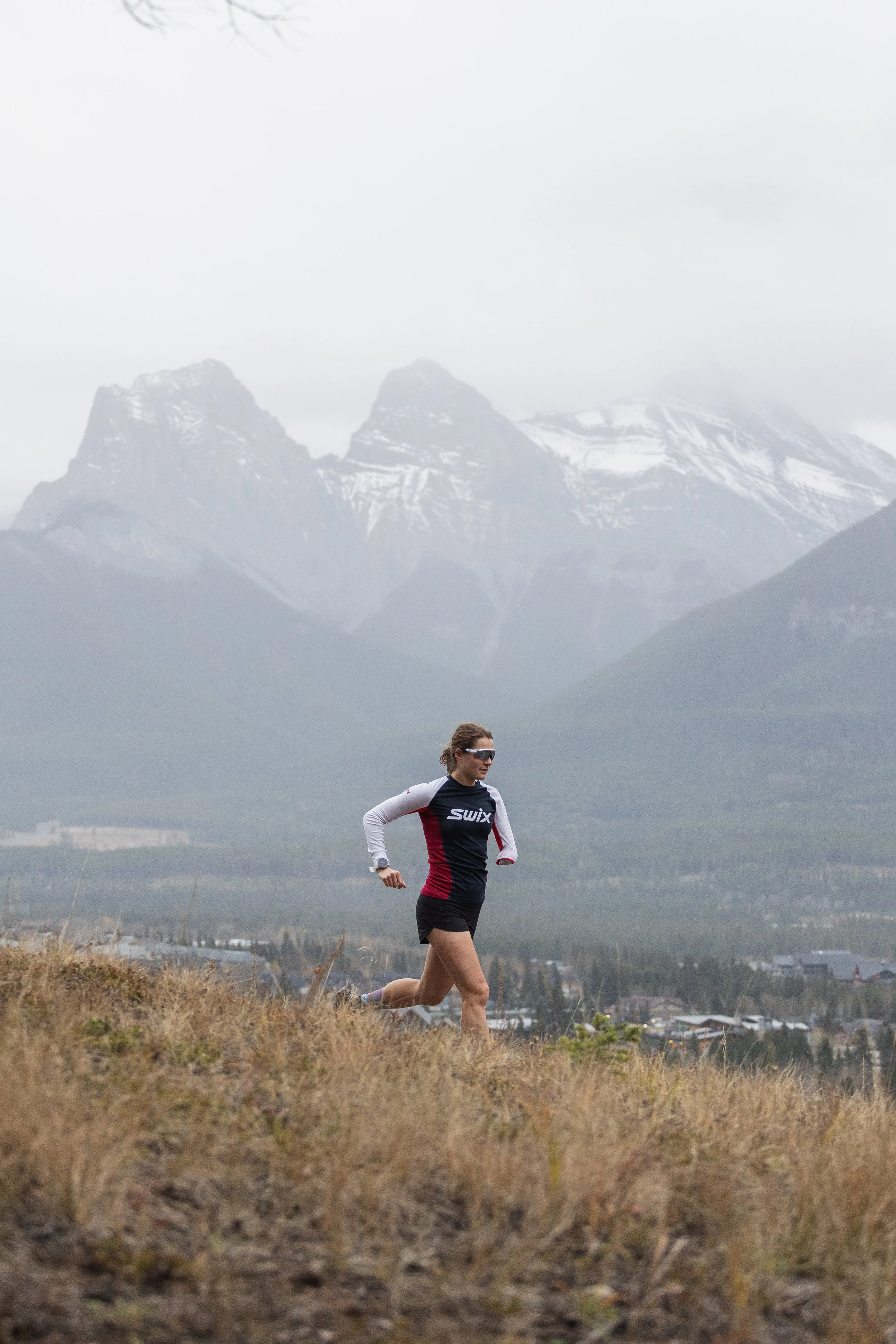 A woman running outdoors in front of snow-capped mountains with a cloudy sky.